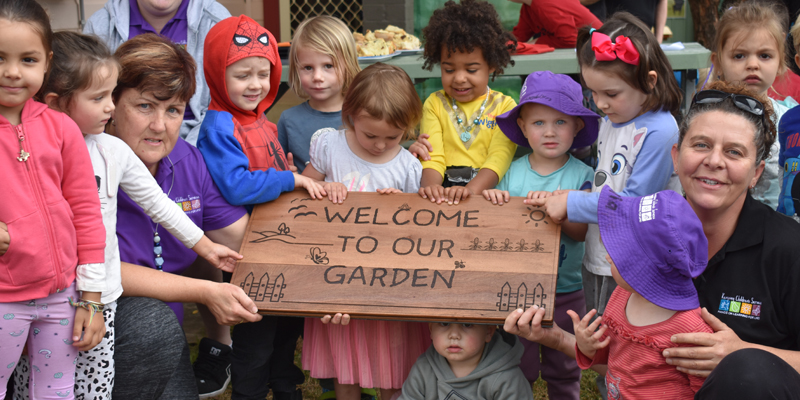 Large group of children holding a sign that says welcome to our garden.